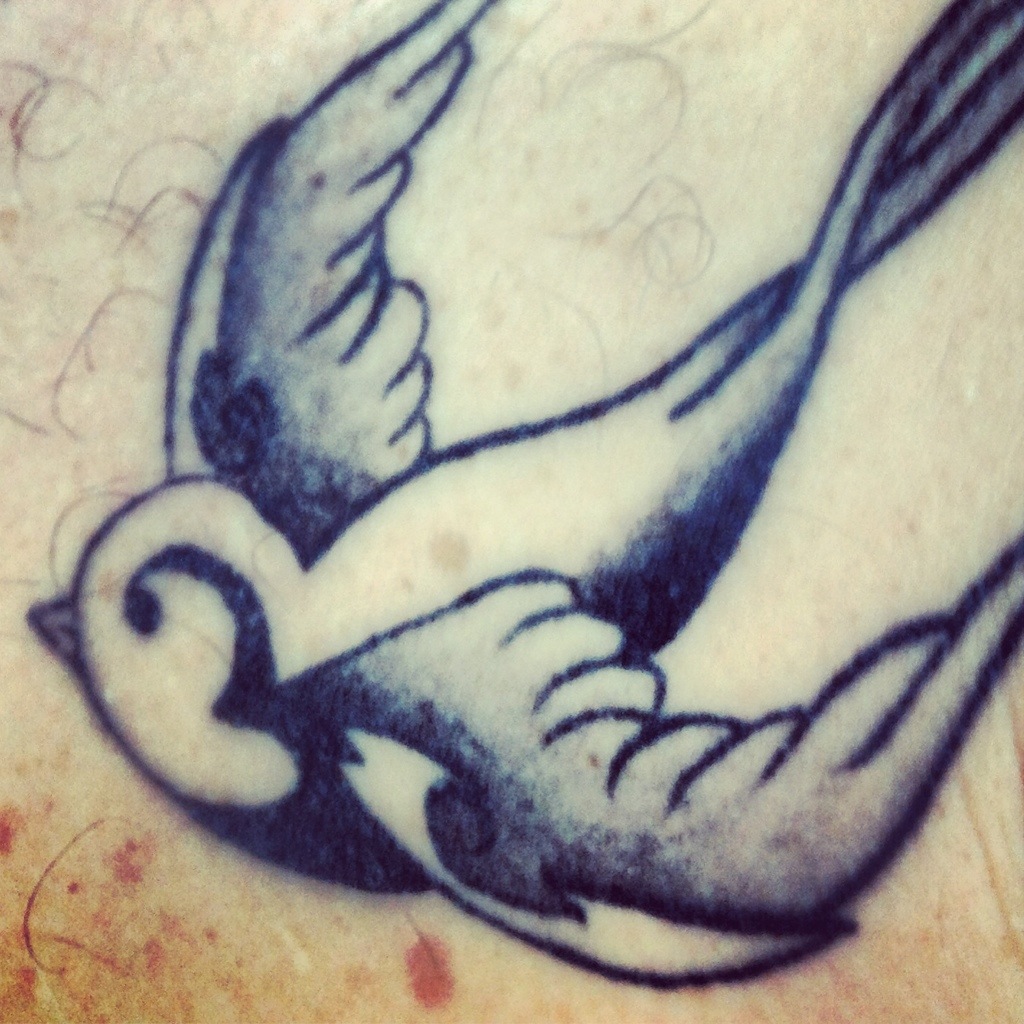 Tatouage hirondelle avec cerise dans le bec